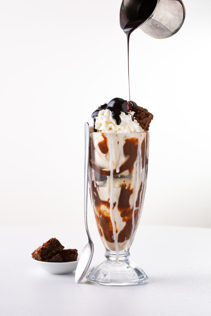A warm, gooey brownie served in a glass, topped with a scoop of chocolate ice cream and drizzled with chocolate syrup